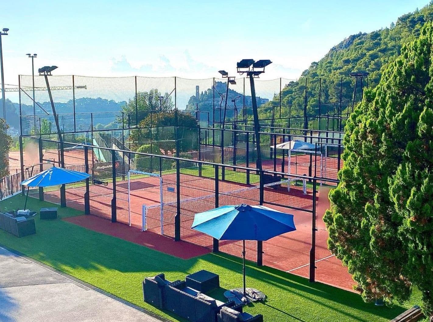 Outdoor padel court with hills and blue umbrellas.