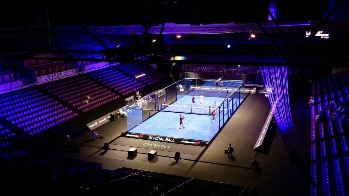 Padel court with players in action, vibrant lighting, and a stadium setting.