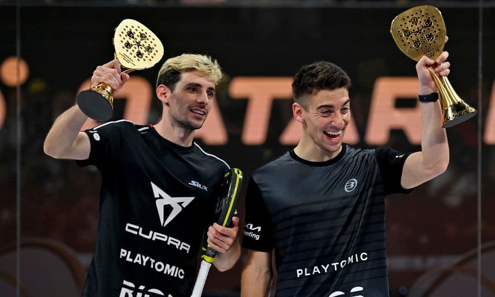 Two individuals holding trophies during the FIP World Padel Championships, wearing black shirts with logos like CUPRA and PLAYTOMIC, standing in front of a backdrop featuring the word "QATAR."