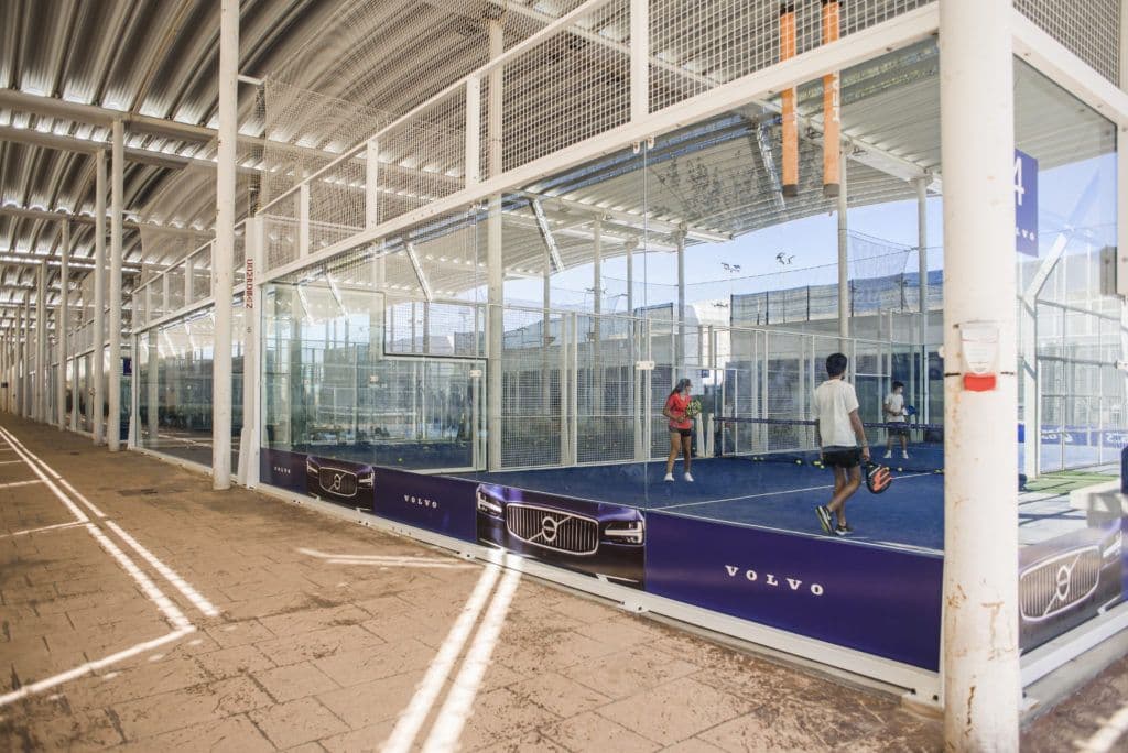 Indoor padel courts with glass walls and Volvo branding.