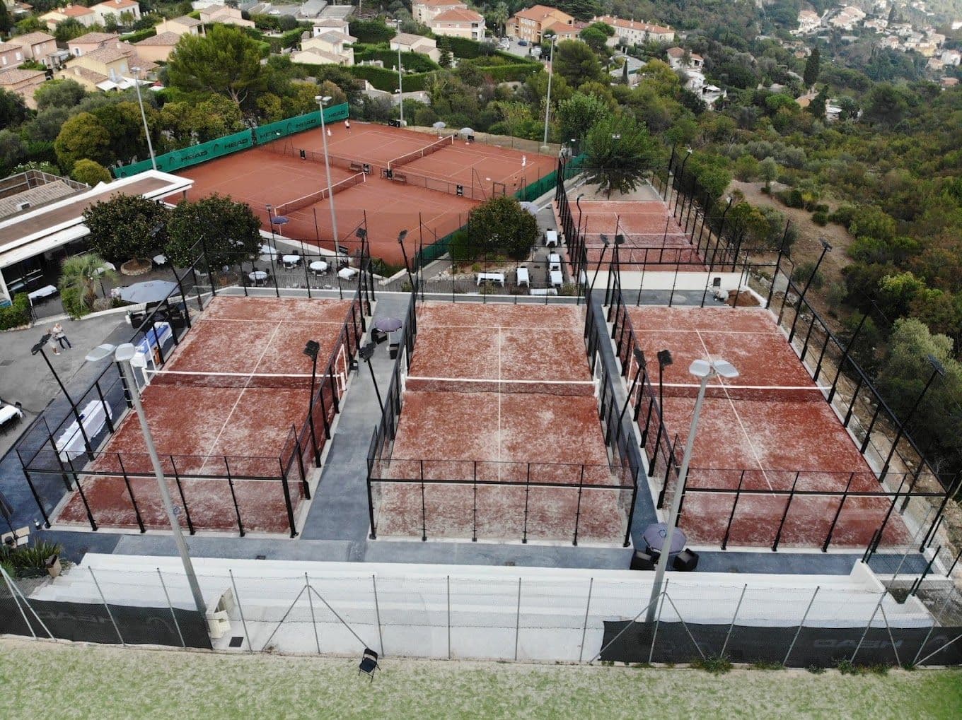 Aerial view of padel courts surrounded by greenery and buildings.
